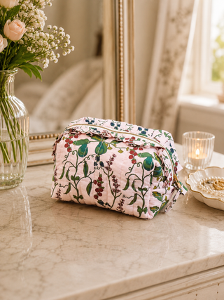 Floral-patterned cosmetic bag on a marble surface with a vase of flowers and candle in the background