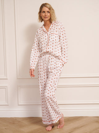 Woman wearing a  heart patterned pyjama set against a white wall.