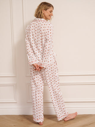 Woman wearing a  heart patterned pyjama set against a white wall.