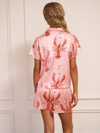 Tween wearing a pink short pyjama set with lobster prints against a white wall. Back Detail