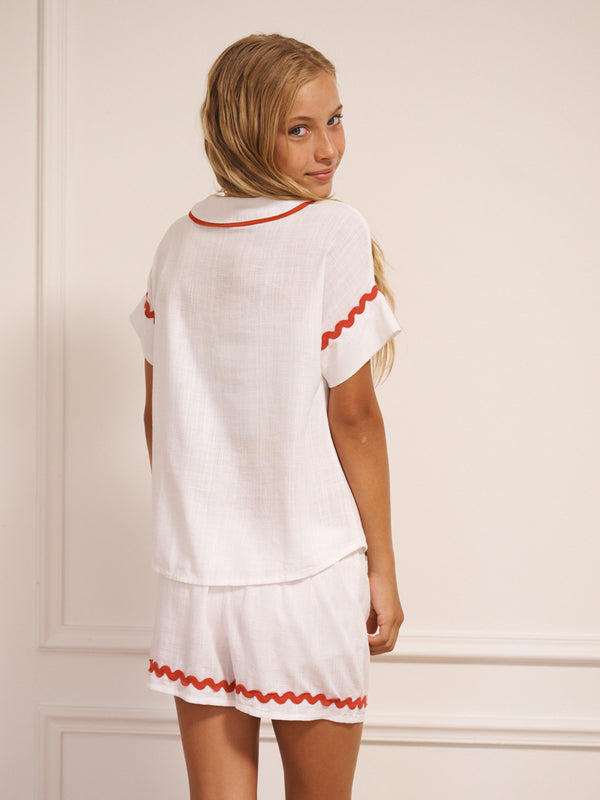 Tween wearing a white pyjama set with red trim against a plain background. Back Detail. 