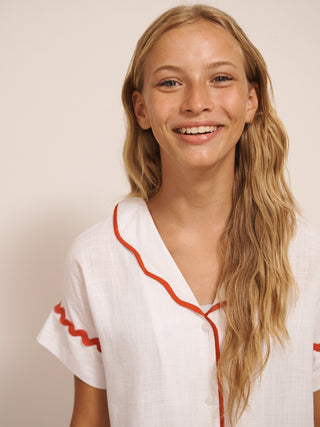 Tween wearing a white pyjama set with red trim against a plain background.