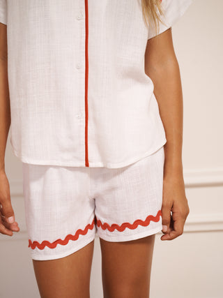 Tween wearing a white pyjama set with red trim against a plain background. Short detail.