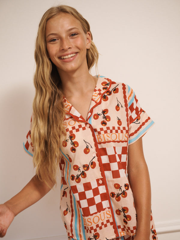 Tween girl wearing a tomato patterned pyjama shirt with checkered design on a plain background