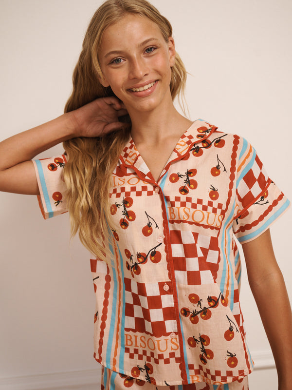 Tween girl wearing a tomato patterned pyjama shirt with checkered design on a plain background