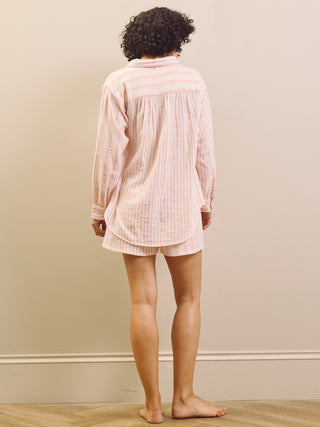 Person wearing a pink strip[ed pyjama set standing against a plain wall.