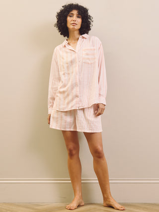 Woman wearing a pink striped short pyjama set against a plain wall.