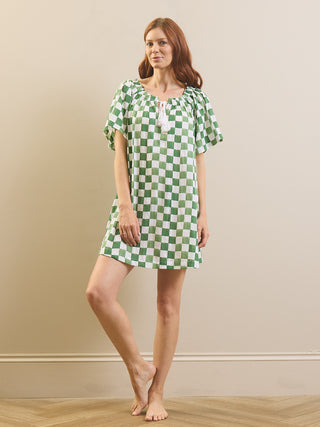 A woman modeling a short-sleeved green and white checkered nightgown against a beige wall and light wood floor.