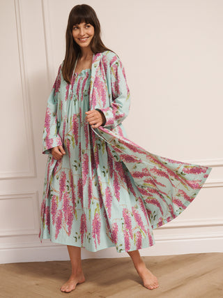 Woman wearing a wisteria floral patterned robe dressing gown in a room with wooden flooring and white walls.
