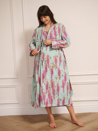 Woman wearing a wisteria floral patterned robe dressing gown in a room with wooden flooring and white walls.