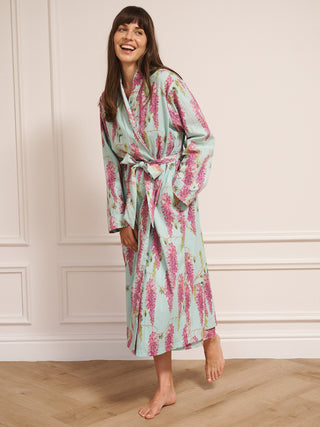 Woman wearing a wisteria floral patterned robe dressing gown in a room with wooden flooring and white walls.