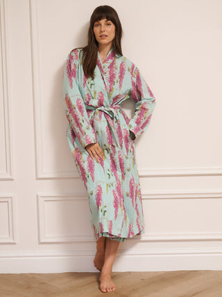 Woman wearing a wisteria floral patterned robe dressing gown in a room with wooden flooring and white walls.