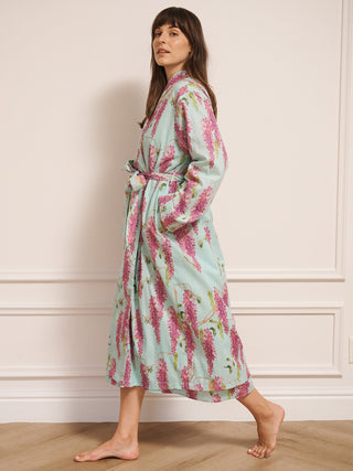 Woman wearing a wisteria floral patterned robe dressing gown in a room with wooden flooring and white walls.