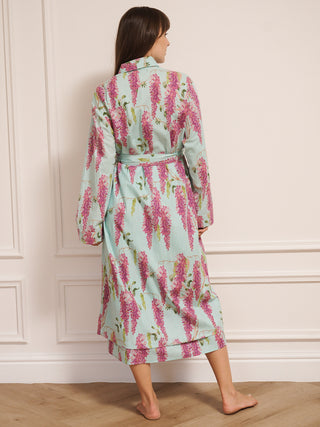 Woman wearing a wisteria floral patterned robe dressing gown in a room with wooden flooring and white walls. Back detail. 
