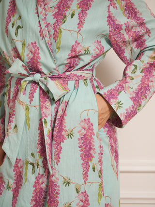 Woman wearing a wisteria floral patterned robe dressing gown in a room with wooden flooring and white walls. Tie detail. 