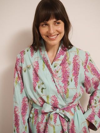 Woman wearing a wisteria floral patterned robe dressing gown in a room with wooden flooring and white walls.