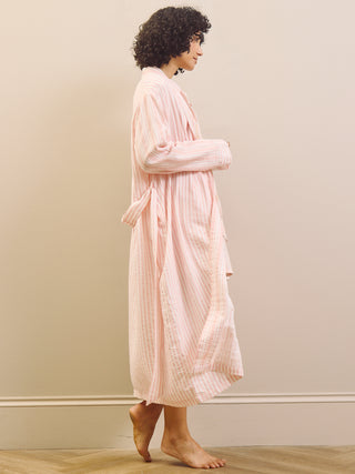 Woman wearing a pink striped pyjama set and robe against a plain background