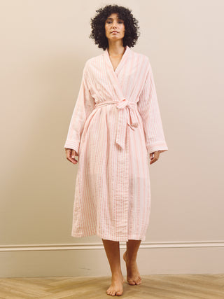 Woman wearing a pink striped pyjama set and robe against a plain background