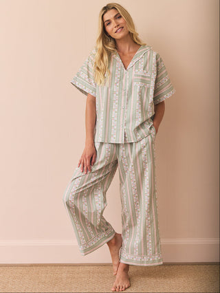 Woman wearing a patterned pyjama set against a beige wall.
