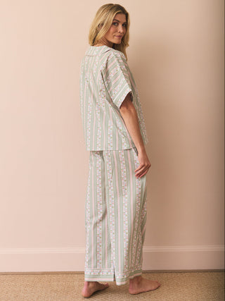 Model wears striped and floral green and pink pyjamas against a plain wall. Back detail. 