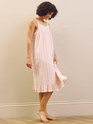 Woman wearing a pink striped nightie dress against a plain wall.