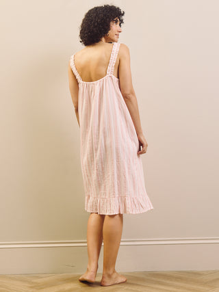 Woman wearing a pink striped dress against a plain wall.