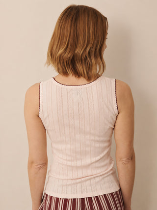 A woman viewed from behind wearing a pale pink ribbed knit sleeveless top with dark red trim, paired with a striped skirt, against a plain beige background.