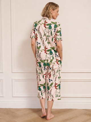 Woman wearing a floral and pear print pyjama set in a room with white walls and wooden flooring.