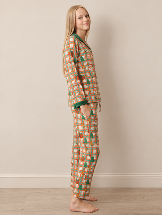 A woman modelling a two-piece pyjama set with a colourful geometric pattern in orange, green, and white, featuring a long-sleeve top and matching pants, standing against a plain beige wall.