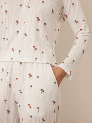 A close-up of a person wearing a white textured long-sleeve top and matching pants with a small red and gray mushroom print, set against a plain beige background.