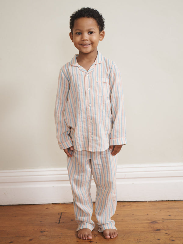Child wearing striped pyjamas standing against a plain wall.