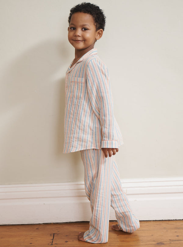 Child wearing a striped pyjama set standing against a plain wall.