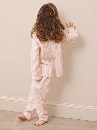 A child wearing a pink and white vertically striped pajama set, shown from behind against a beige wall and light wood floor.