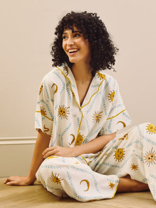 Woman wearing a cream pyjama set with sun and moon patterns sat on the floor in a minimal indoor setting
