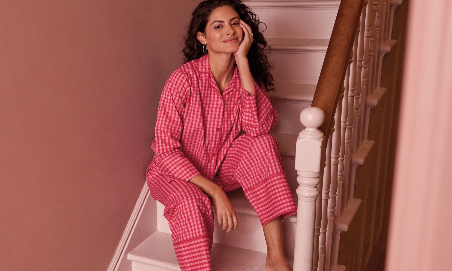 Woman in pink checkered gingham pyjamas sitting on a staircase.