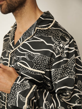 A close-up of a man wearing a black long-sleeve pyjama shirt with a white hand-drawn style animal and wavy line pattern, featuring cream-colored piping.