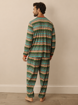 A man wearing a long-sleeve pyjama set with a green, teal, and orange geometric pattern, shown from the back against a beige wall and wood floor.