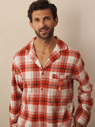 A man wearing a red and white plaid long-sleeve pyjama shirt with a chest pocket, posed against a plain beige background.