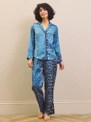 A woman modelling a two-piece pyjama set with a blue and white abstract fawn pattern, standing against a beige wall on a light wood floor.