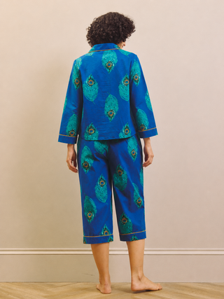 Model wears a pair of navy peacock print capri pyjamas against a beige wall