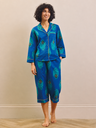 Woman wearing a blue peacock patterned capri pyjama set against a beige wall.