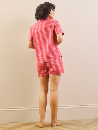 Model wearing a pink gingham pyjama set against a beige wall. Back Detail