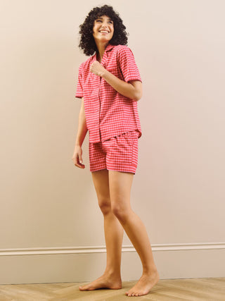 Model wearing a pink gingham pyjama set against a beige wall.