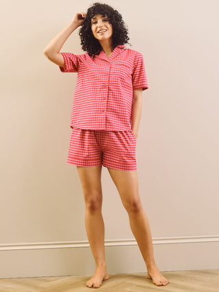 Model wearing a pink gingham pyjama set against a beige wall.