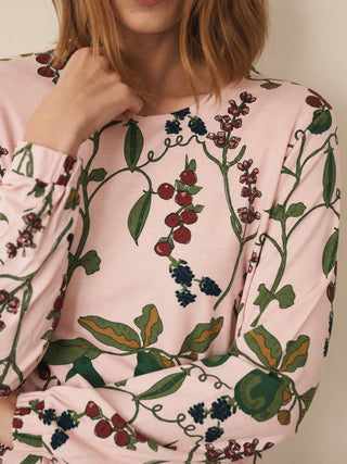 A close-up of a woman wearing a light pink long-sleeve pyjama top with a detailed botanical print of green vines, leaves, and clusters of red and dark blue berries.