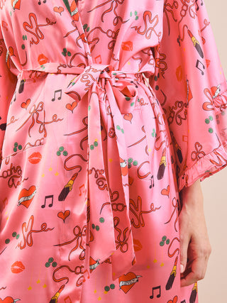 A close-up of a pink satin robe with a tie waist, featuring a playful print of lips, hearts, lipstick tubes, music notes, and the word 'Love' in script, with a hand visible at the side.