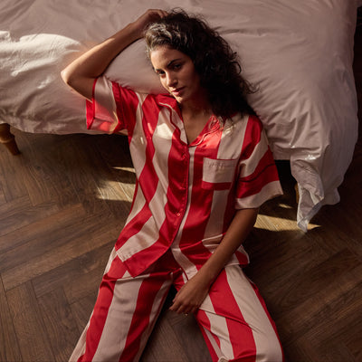Woman wearing a red and white striped pyjamas sitting on the floor in a bedroom.