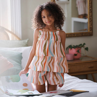 Young girl in a colourful striped pyjamas standing on a bed with books and a plant in the background.