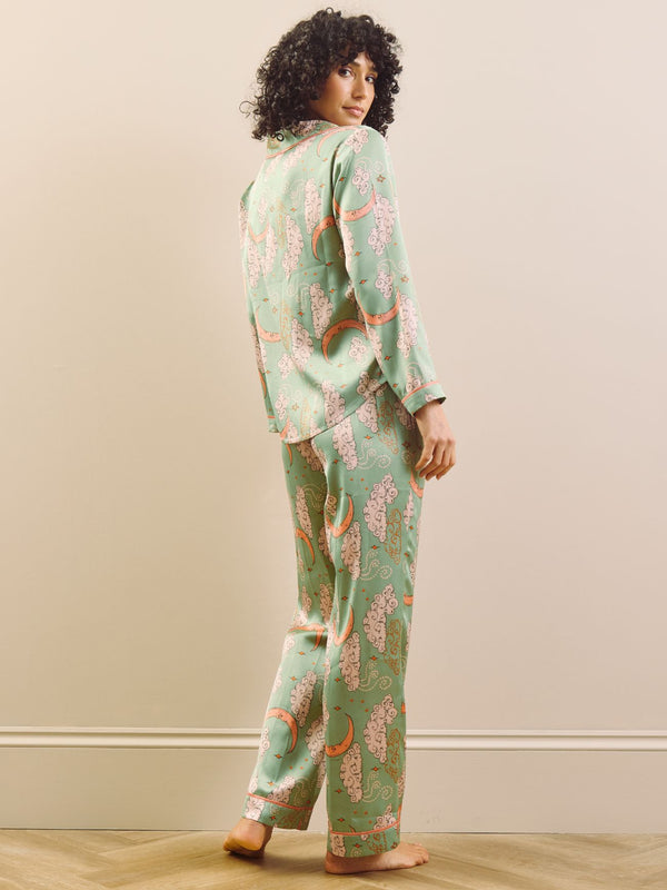 Model wearing a green moon and clouds design long satin pyjama set against a beige background. Back Detail. 