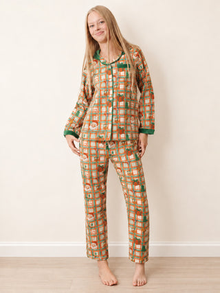 A teenage girl modelling a two-piece long-sleeve pyjama set with a retro geometric pattern in orange, green, and beige, standing against a plain beige wall.